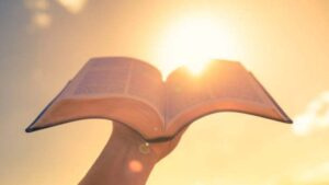A person holds an open book toward a bright sun.